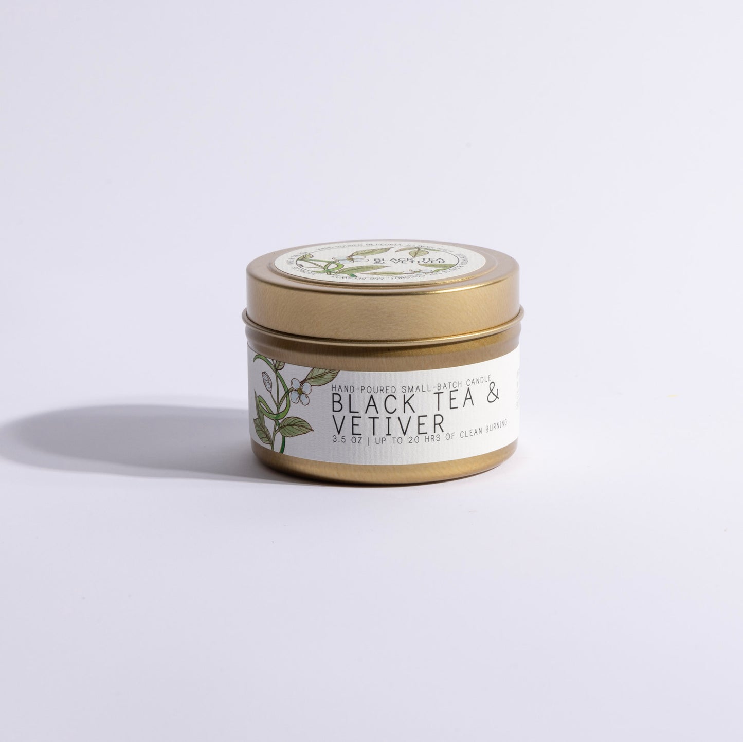 A gold-lidded candle jar labeled 'Black Tea & Vetiver' on a light background.
