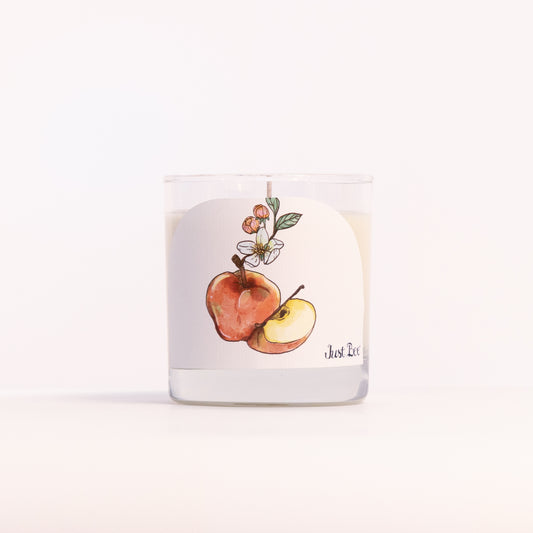 Just Bee Apple Harvest candle in a clear glass jar, apple label facing forward in a closer view.
