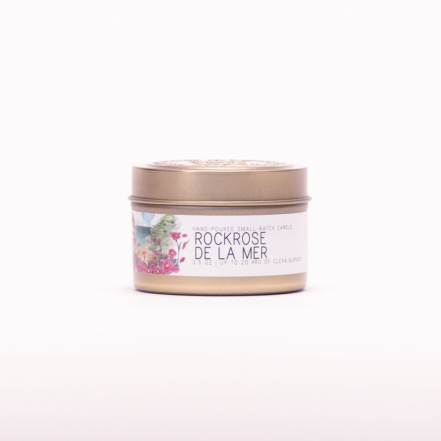 Just Bee Rockrose de la Mer candle in a closed gold travel tin, pink rockrose label facing forward.