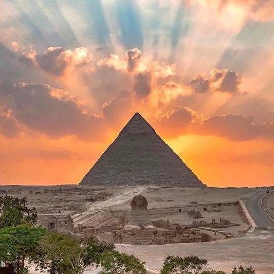 Silhouette of an Egyptian pyramid at sunset with sun rays breaking through clouds