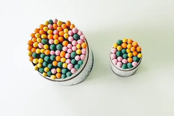 Two tins of Just Bee pastel-tipped safety matches in pink, orange, green and yellow, one large and one small