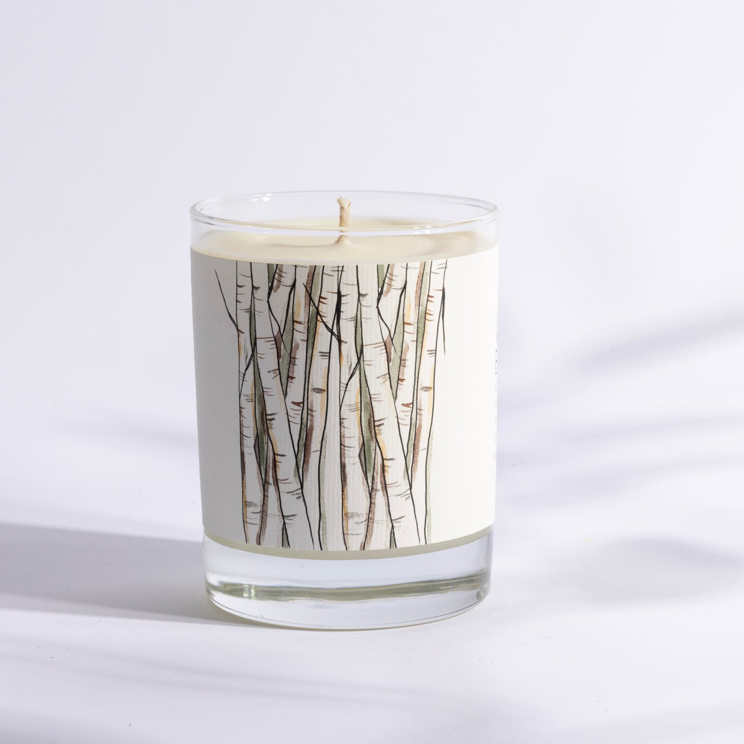 A candle in a glass holder featuring a design of birch tree branches.