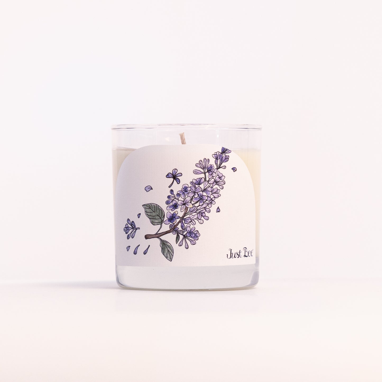 Just Bee Lilac candle in a clear glass jar, purple lilac label facing forward in a closer view.