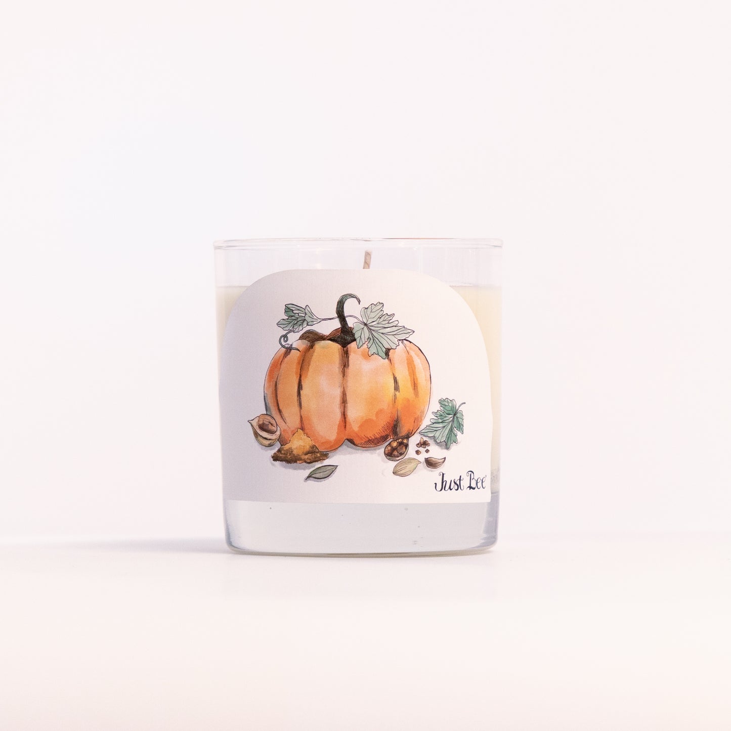 Just Bee Spiced Pumpkin candle in a clear glass jar, pumpkin label facing forward in a closer view.