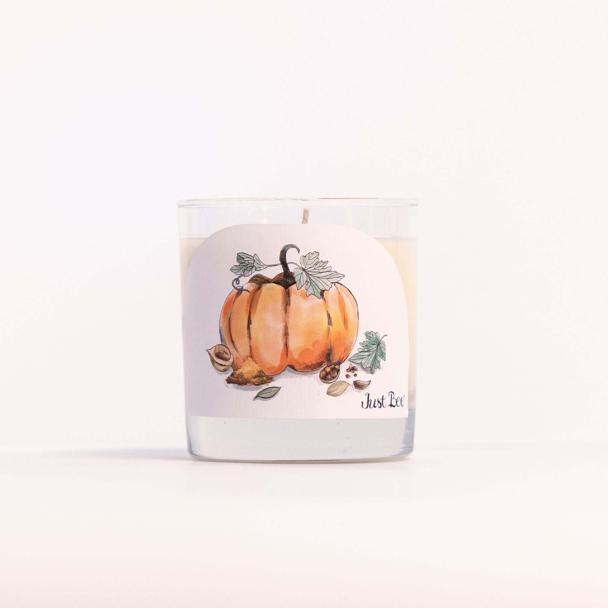 Just Bee Spiced Pumpkin candle in a clear glass jar, pumpkin label facing forward in a closer view.