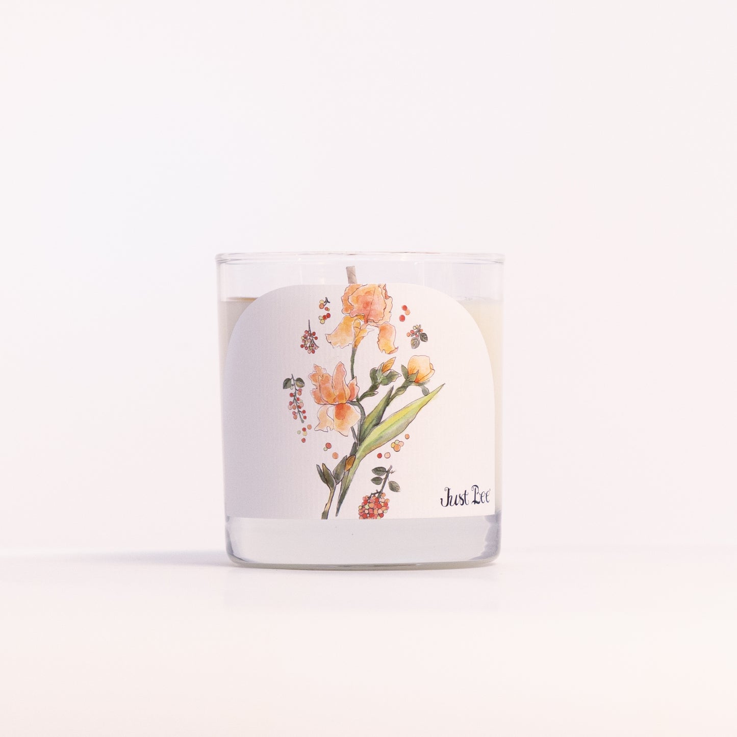 Just Bee Iris & Pink Peppercorn candle in a clear glass jar, iris label facing forward in a closer view.