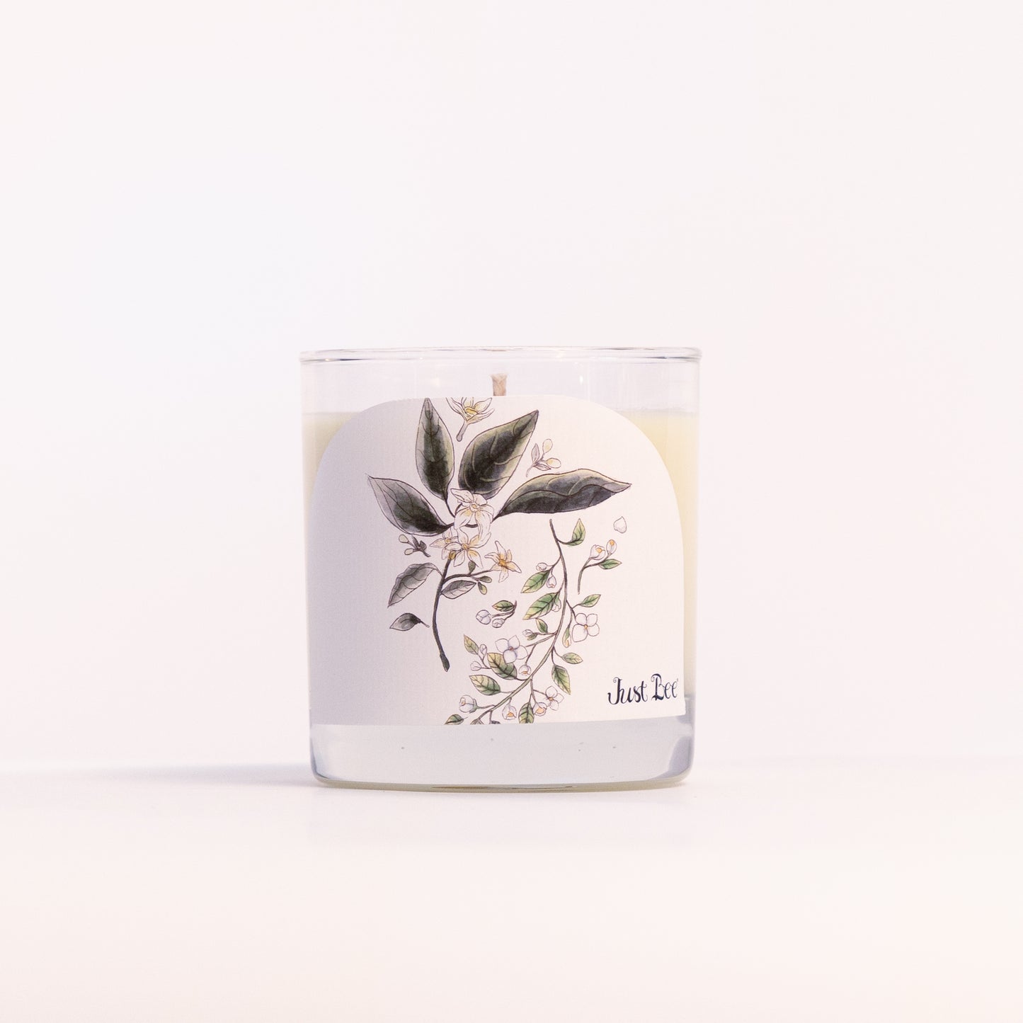 Just Bee Jasmine & Orange Blossom candle in a clear glass jar, blossom label facing forward, closer view.