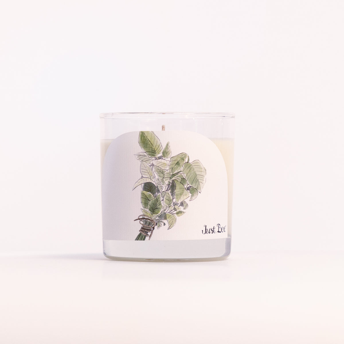 Just Bee Summer Mint candle in a clear glass jar, mint sprig label facing forward in a closer view.