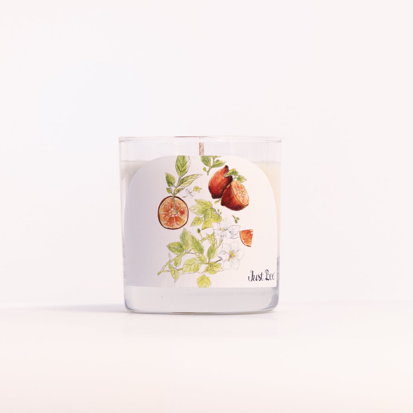 Just Bee Blood Lime & Green Tea candle in a clear glass jar, blood lime label facing forward, closer view.