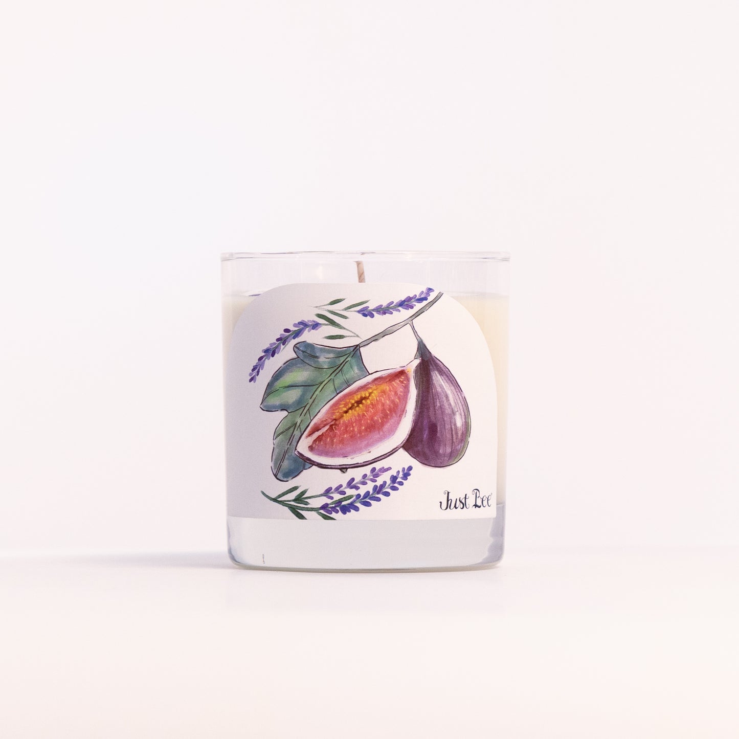 Just Bee Lavender Fig candle in a clear glass jar, fig and lavender label facing forward, closer view.