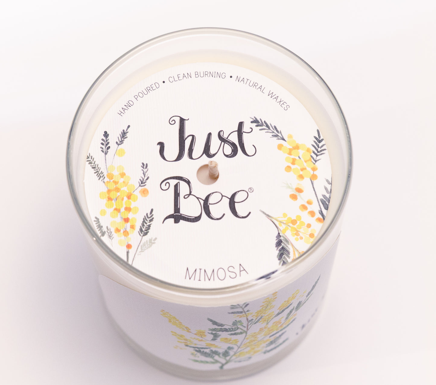 Just Bee Mimosa candle from above, round lid label with yellow mimosa sprays and a centered wick.
