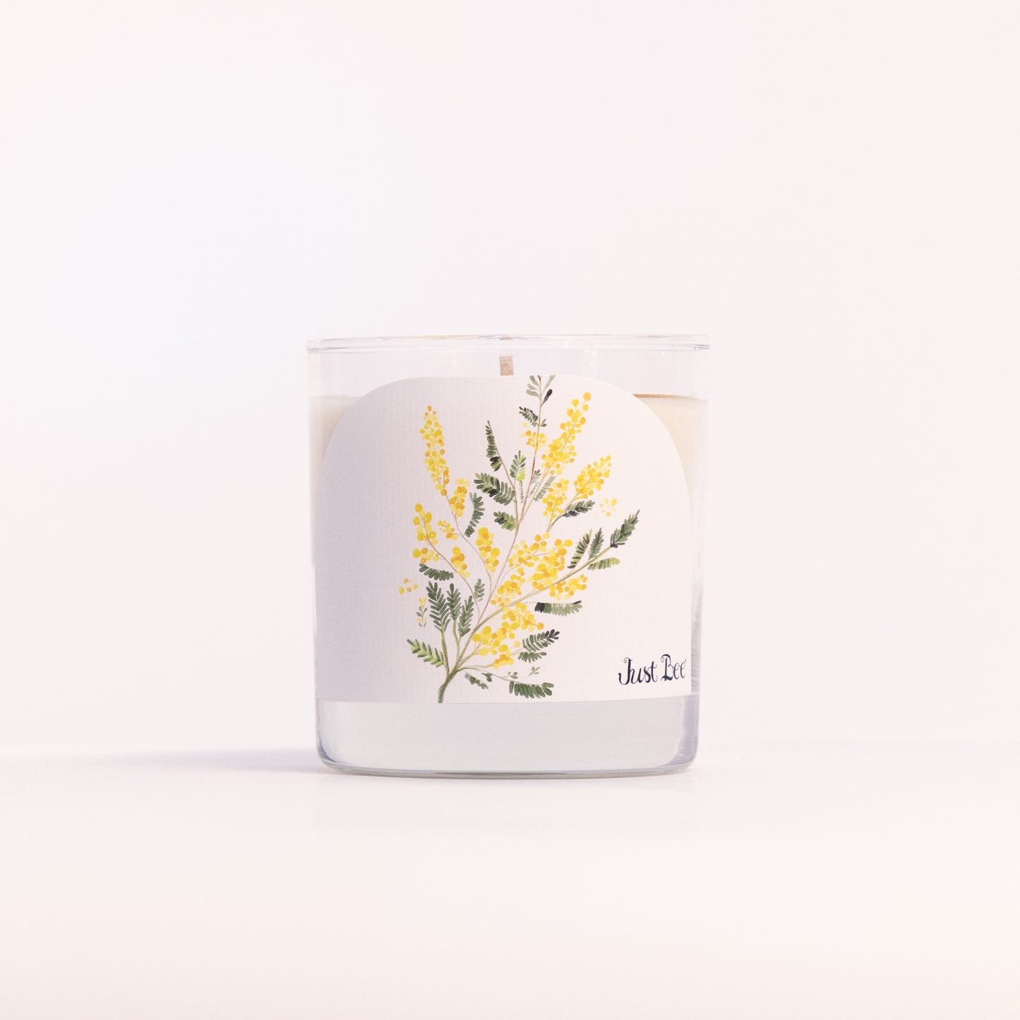 Just Bee Mimosa candle in a clear glass jar, yellow mimosa label facing forward in a closer view.