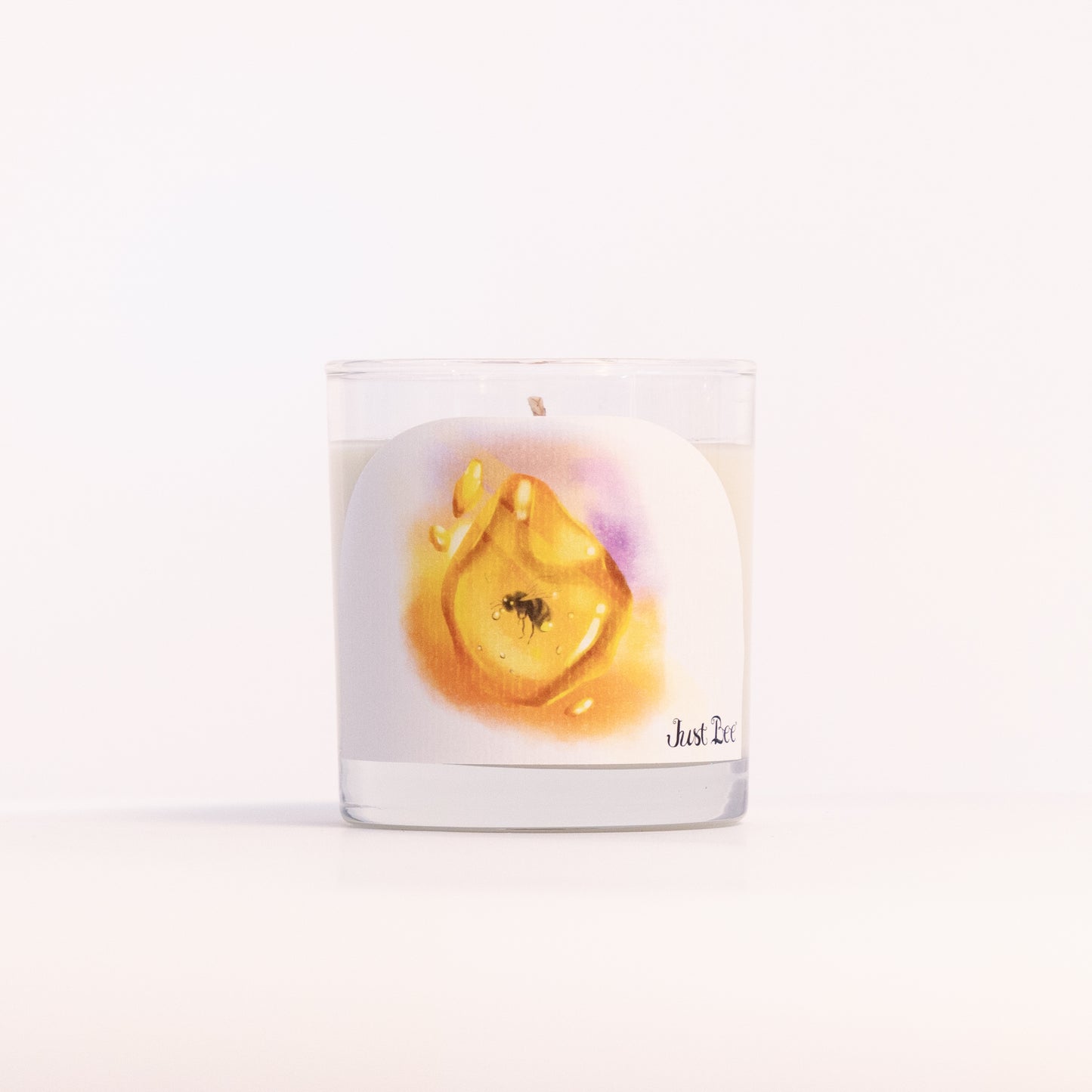 Just Bee Golden Amber candle in a clear glass jar, amber resin label facing forward in a closer view.
