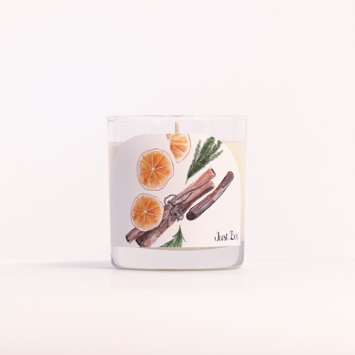 Just Bee Christmas Hearth candle in a clear glass jar, orange and cinnamon label facing forward, closer view.