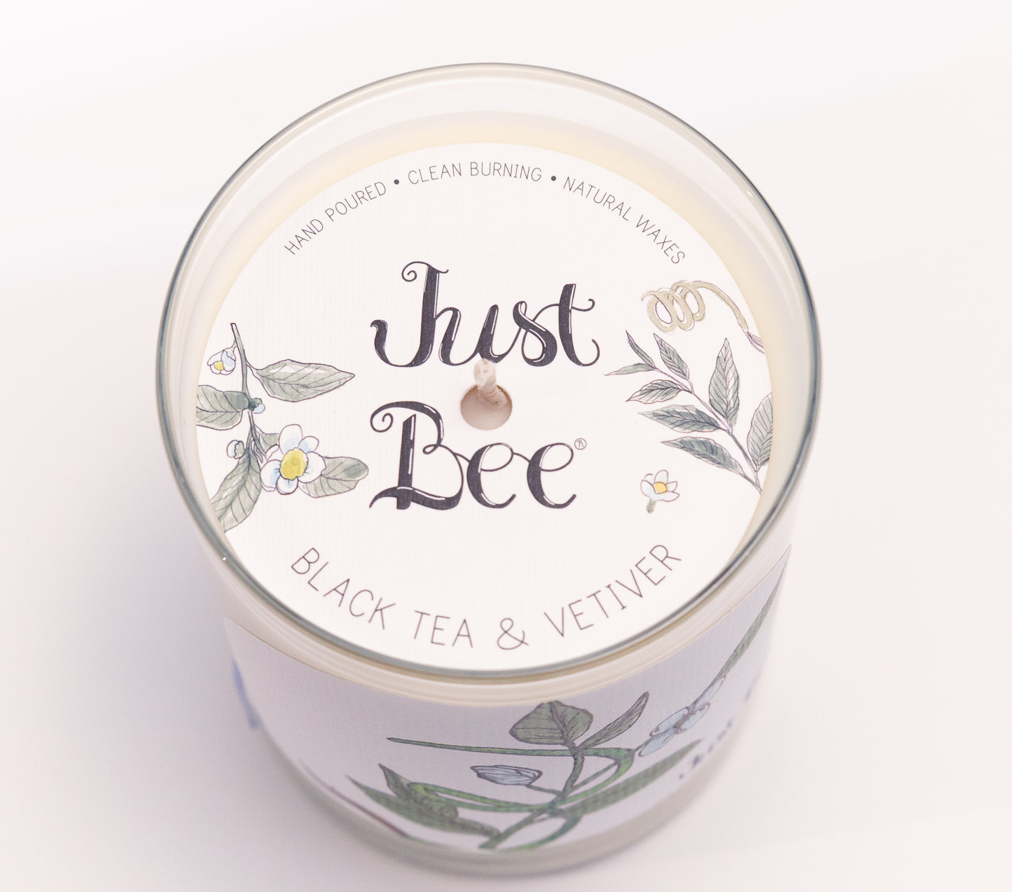 Just Bee Black Tea & Vetiver candle from above, round lid label with tea leaves and a centered wick.