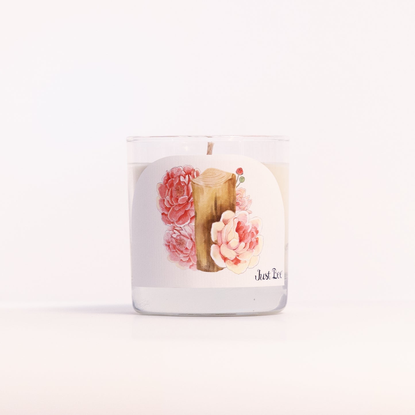 Just Bee Peony & Mahogany candle in a clear glass jar, peony label facing forward in a closer view.