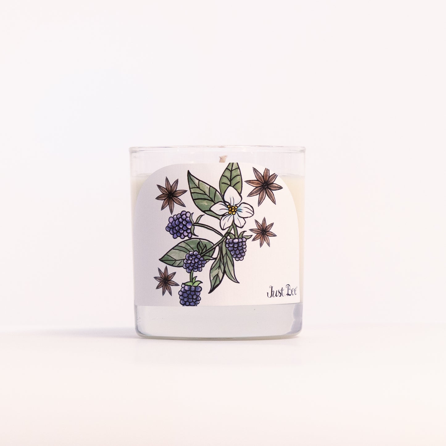 Just Bee Blackberry Anise candle in a clear glass jar, blackberry label facing forward in a closer view.