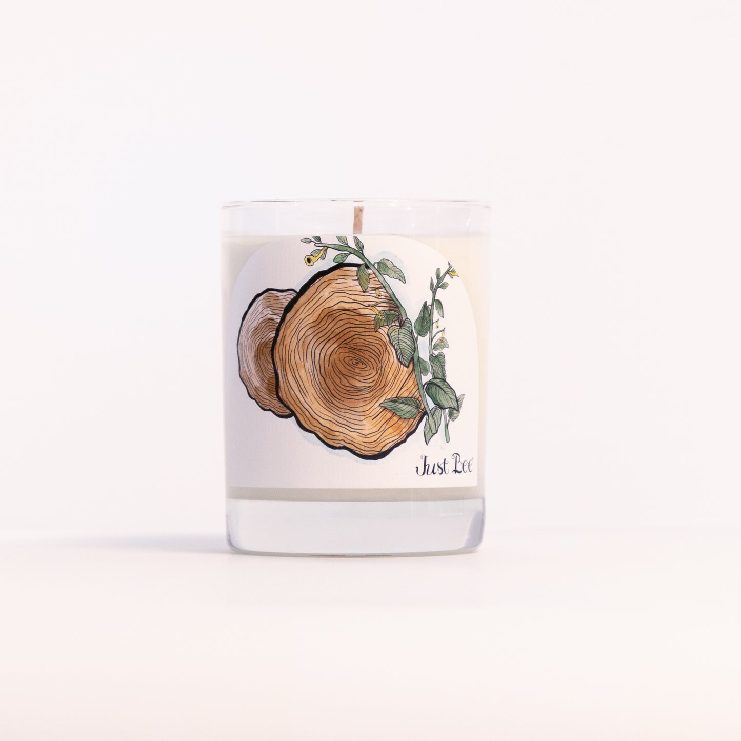 Just Bee Teakwood Tobacco candle in a clear glass jar illustrated with a cut wood slice and eucalyptus.
