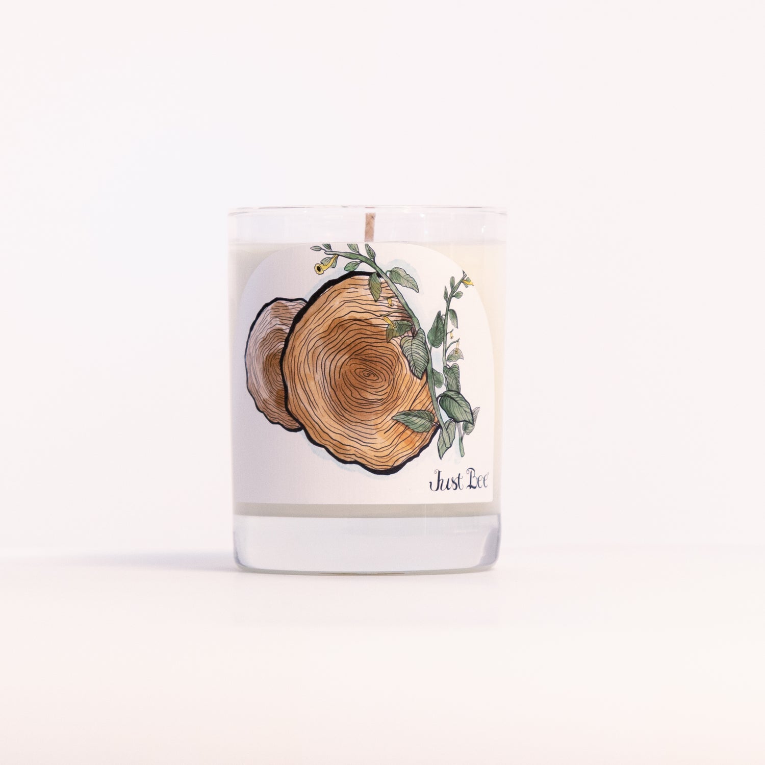 Just Bee Teakwood Tobacco candle in a clear glass jar illustrated with a cut wood slice and eucalyptus.