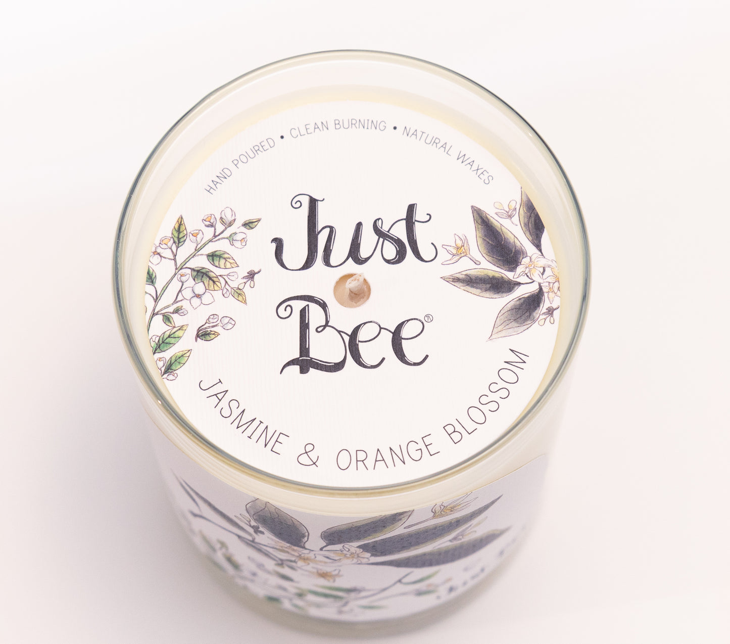 Just Bee Jasmine & Orange Blossom candle from above, round lid label with white blossoms and a centered wick.