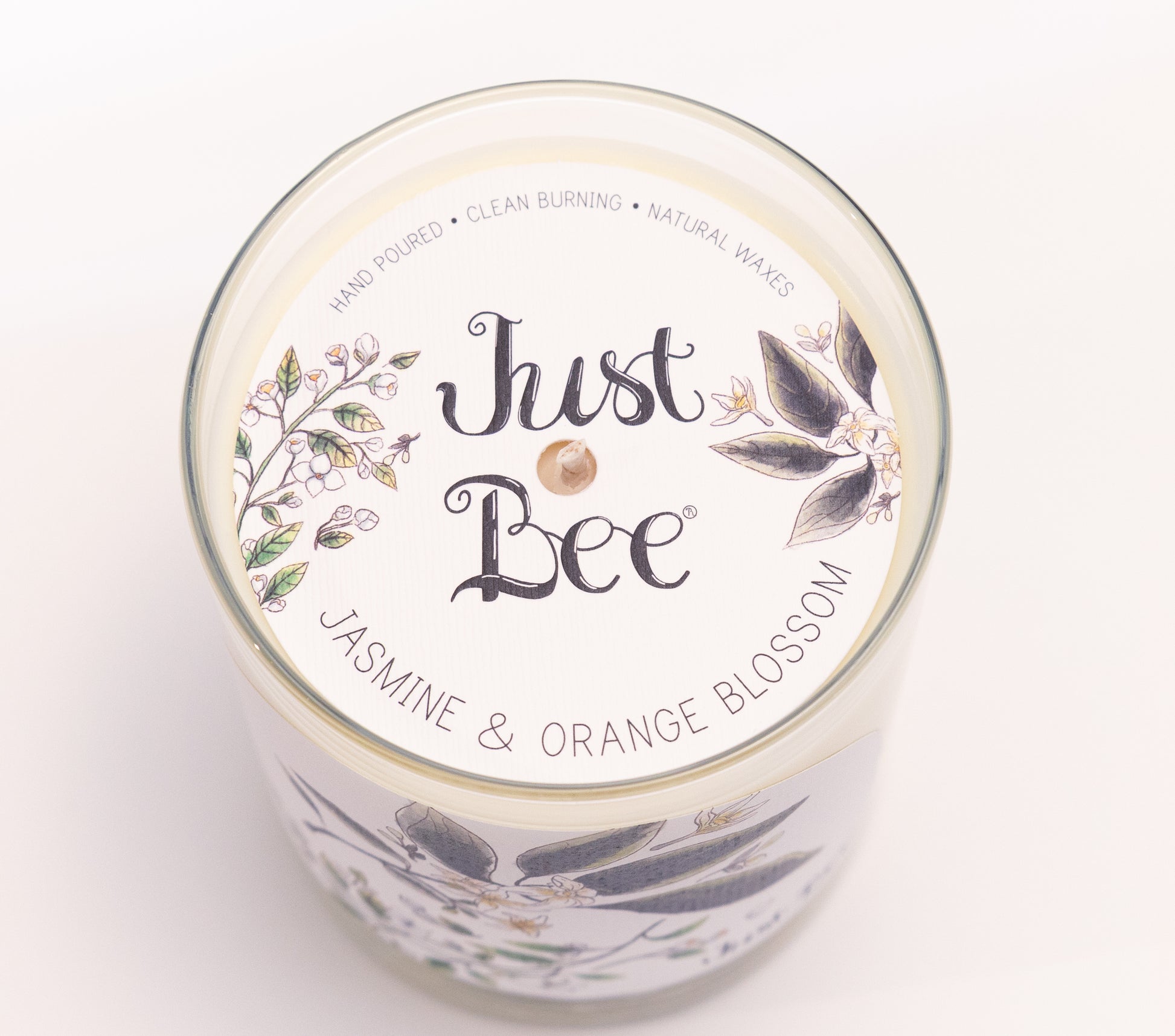 Just Bee Jasmine & Orange Blossom candle from above, round lid label with white blossoms and a centered wick.