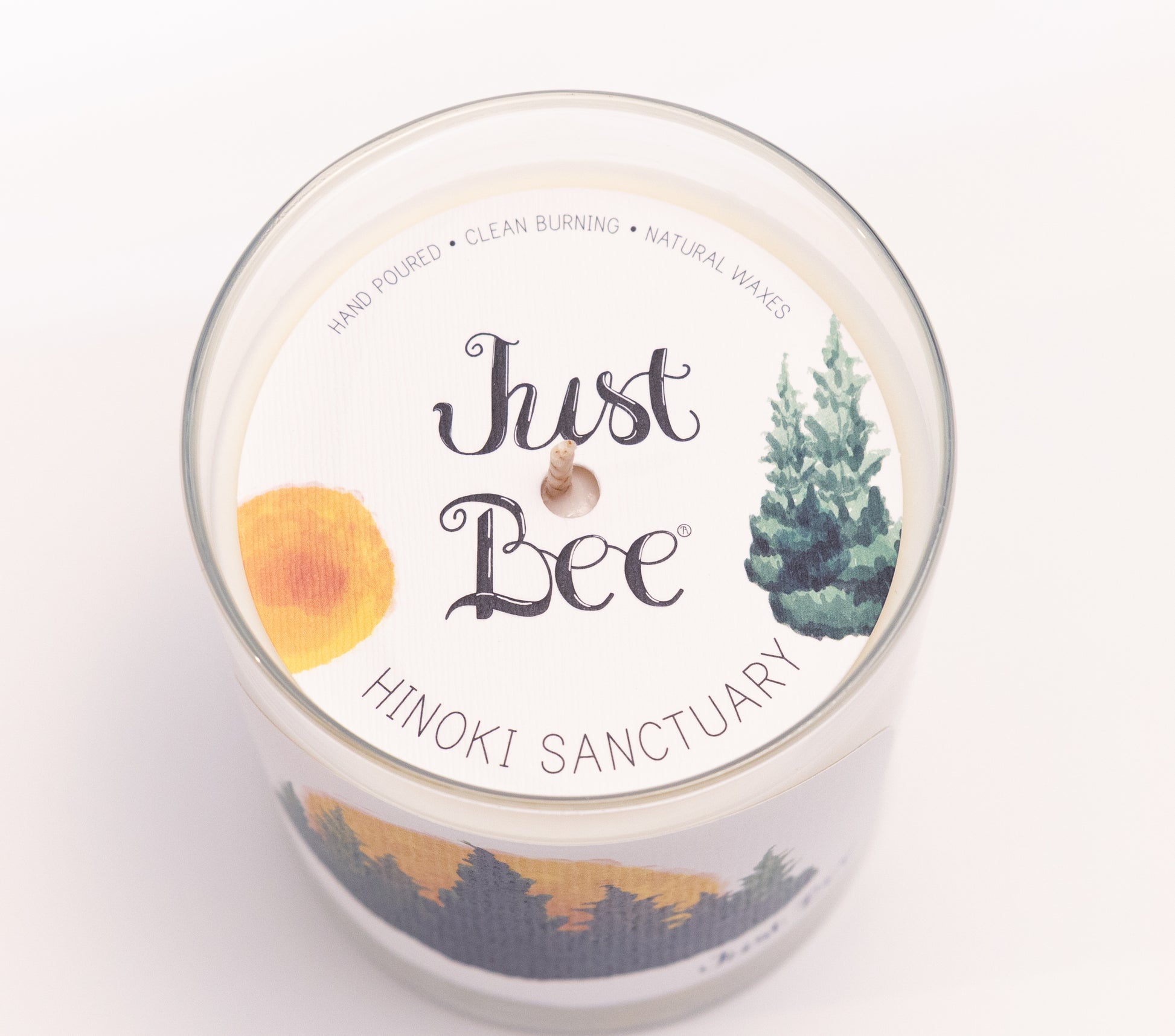 Just Bee Hinoki Sanctuary candle from above, round lid label with pine trees and a centered wick.