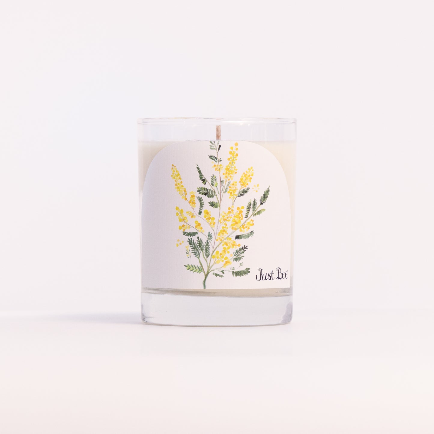 Just Bee Mimosa candle in a clear glass jar illustrated with sprays of yellow mimosa blossoms.