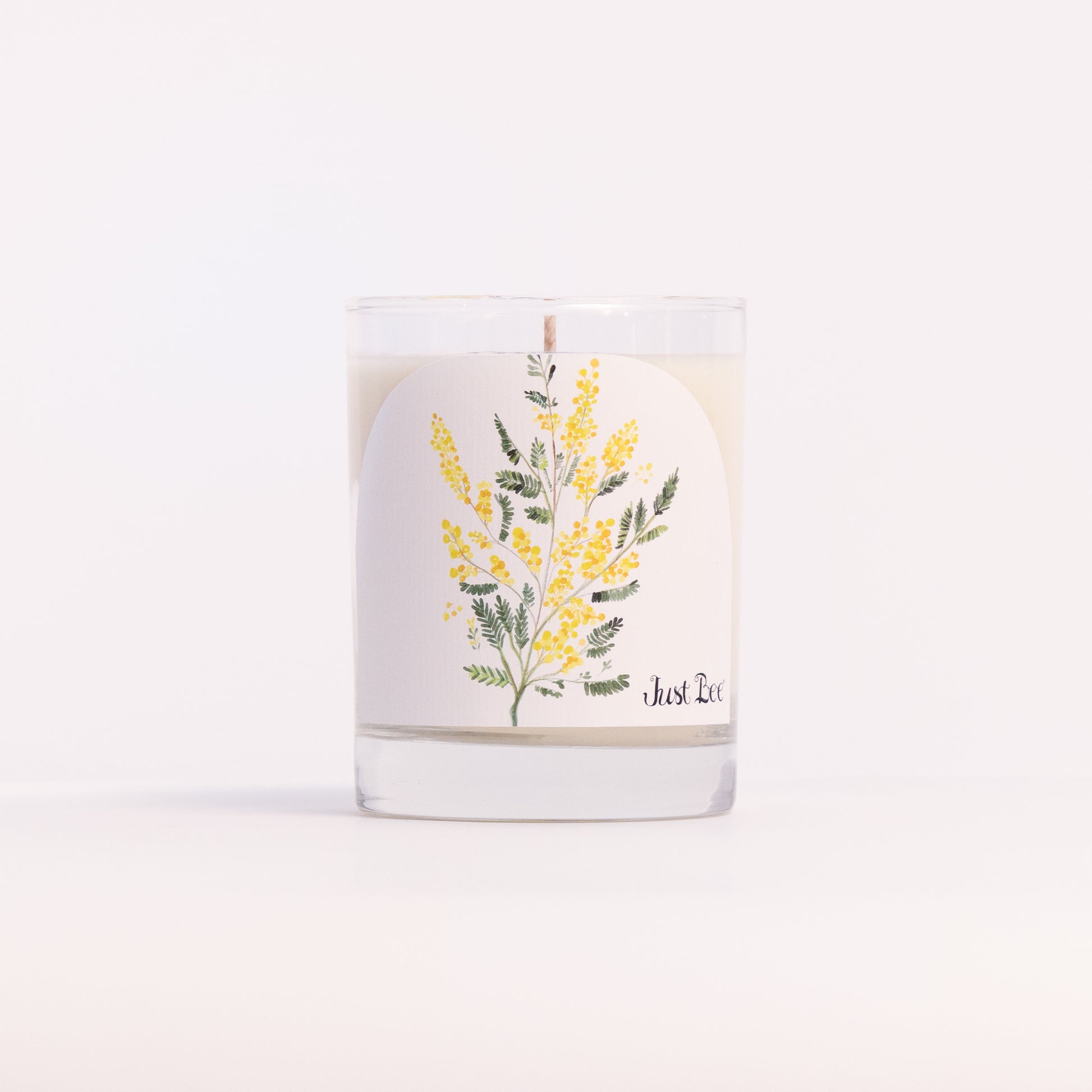 Just Bee Mimosa candle in a clear glass jar illustrated with sprays of yellow mimosa blossoms.