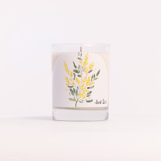 Just Bee Mimosa candle in a clear glass jar illustrated with sprays of yellow mimosa blossoms.
