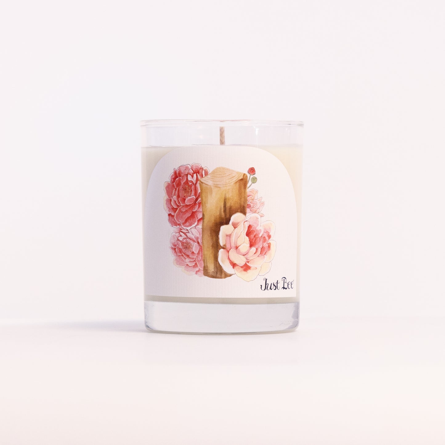 Just Bee Peony & Mahogany candle in a clear glass jar illustrated with pink peonies and a mahogany plank.