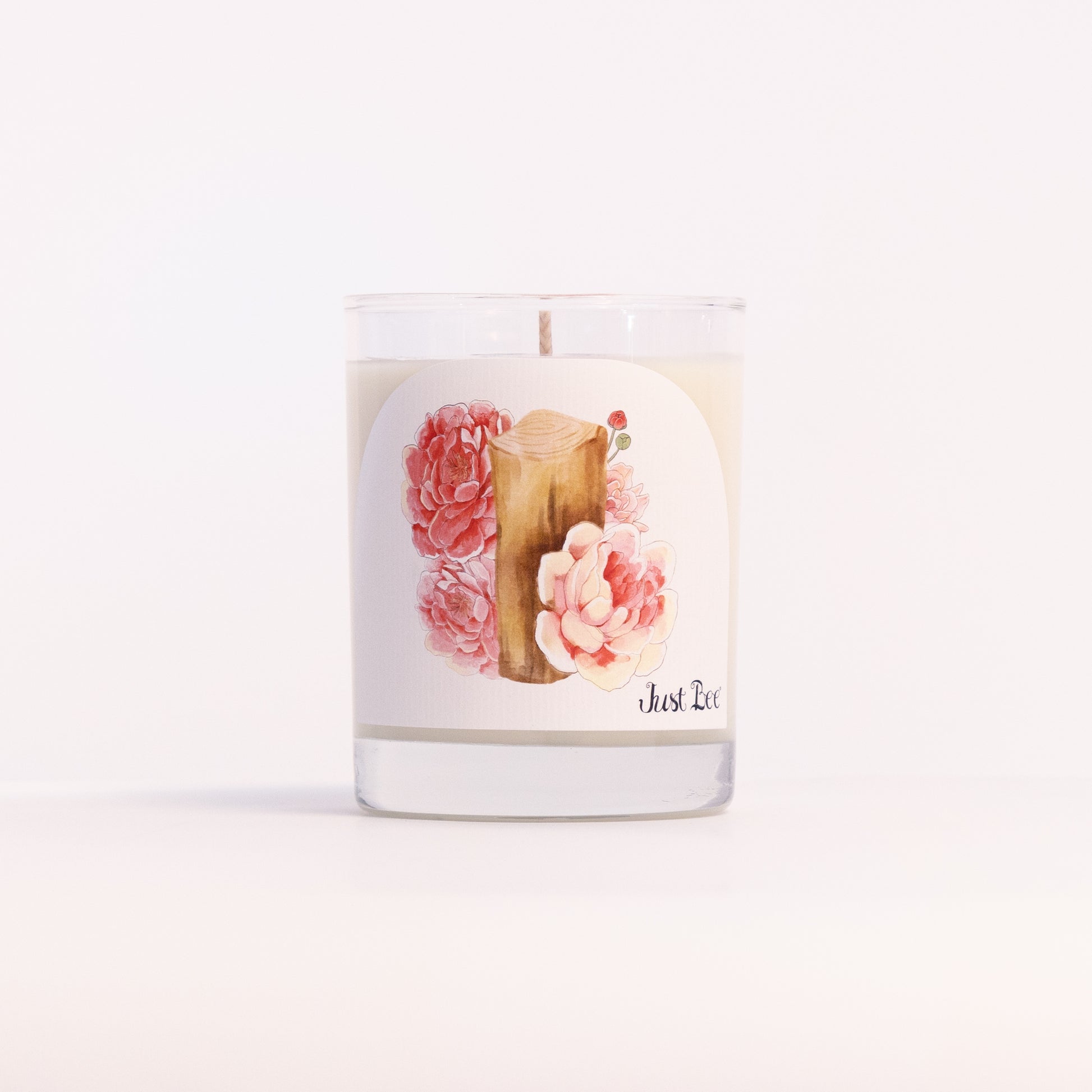 Just Bee Peony & Mahogany candle in a clear glass jar illustrated with pink peonies and a mahogany plank.