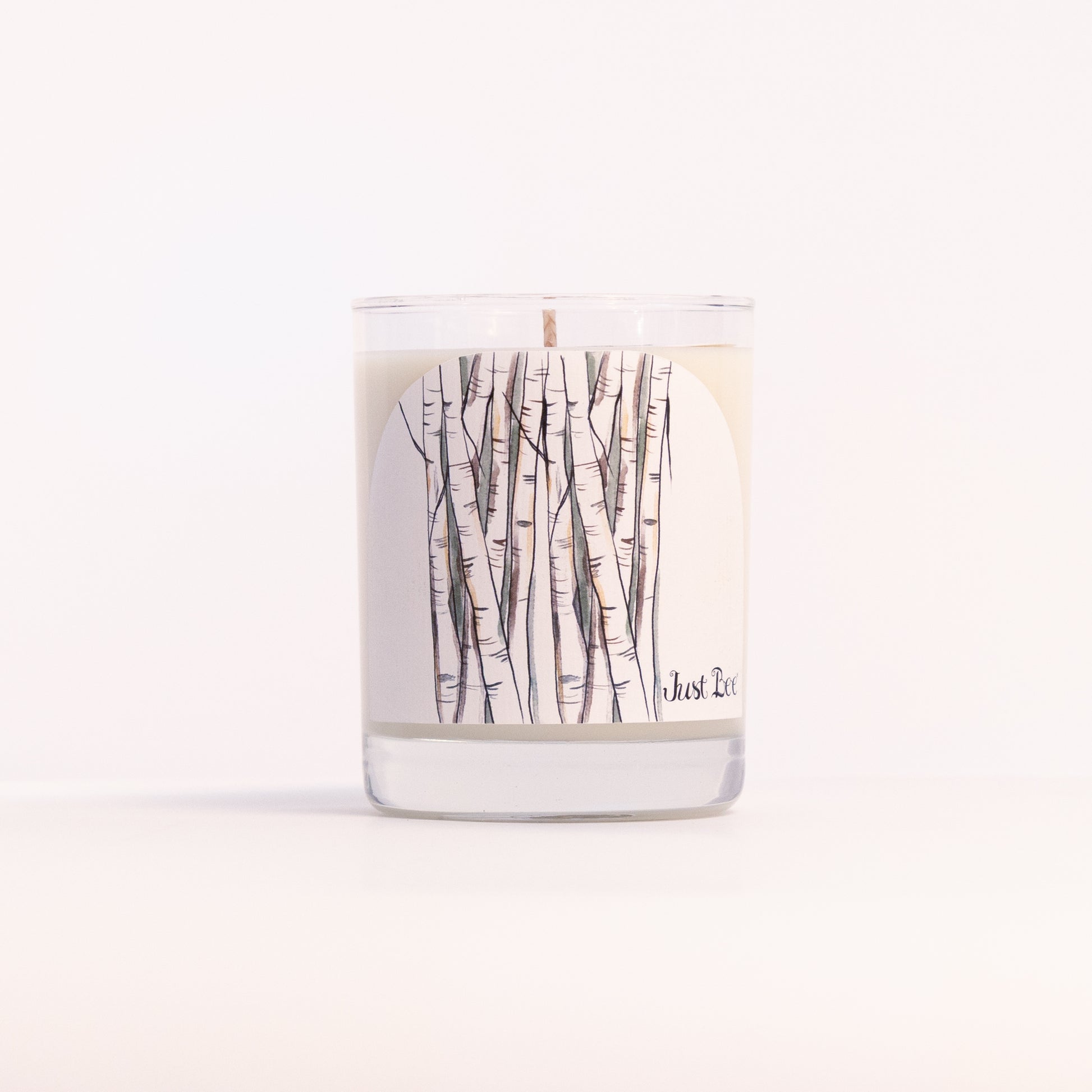 Just Bee White Birch candle in a clear glass jar wrapped with a slender birch trunk illustration, front view.