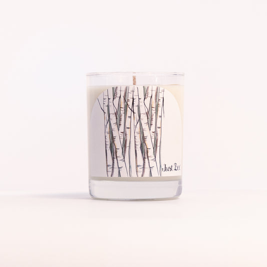 Just Bee White Birch candle in a clear glass jar wrapped with a slender birch trunk illustration, front view.
