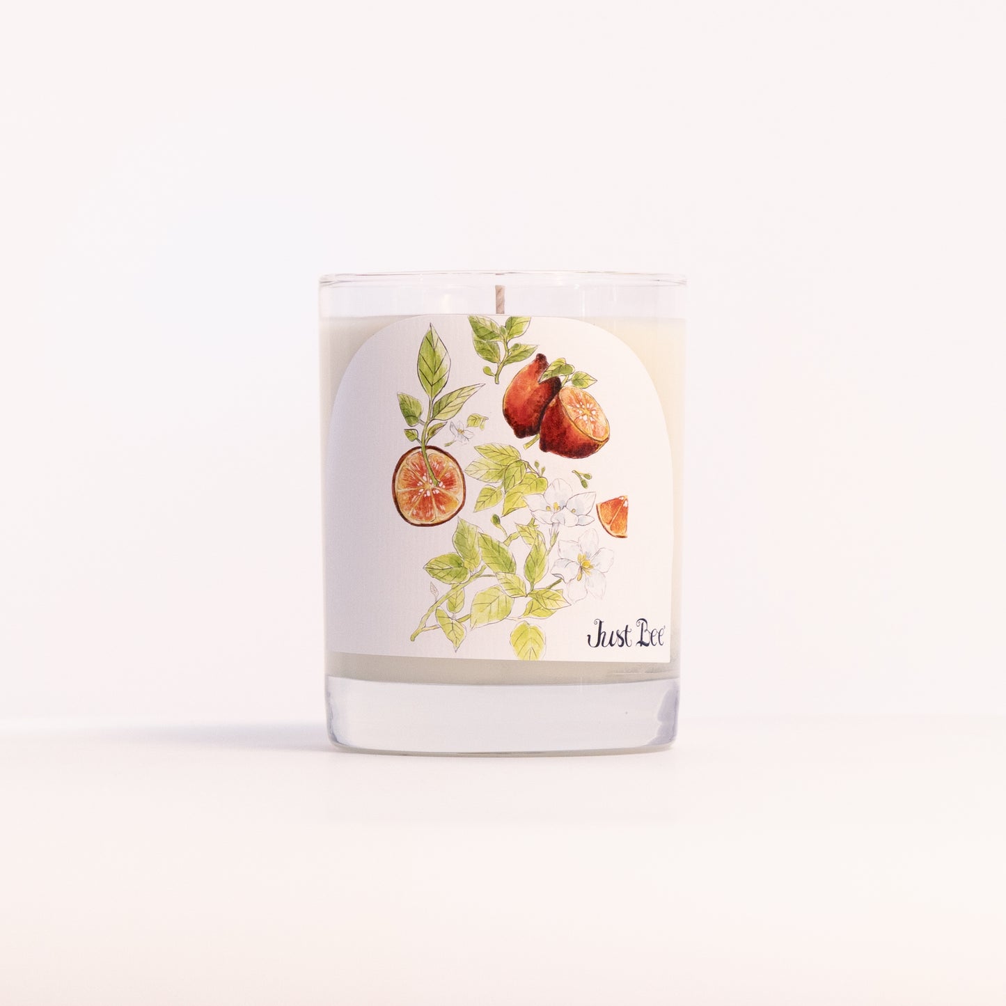 Just Bee Blood Lime & Green Tea candle in a clear glass jar illustrated with halved limes and tea leaves.
