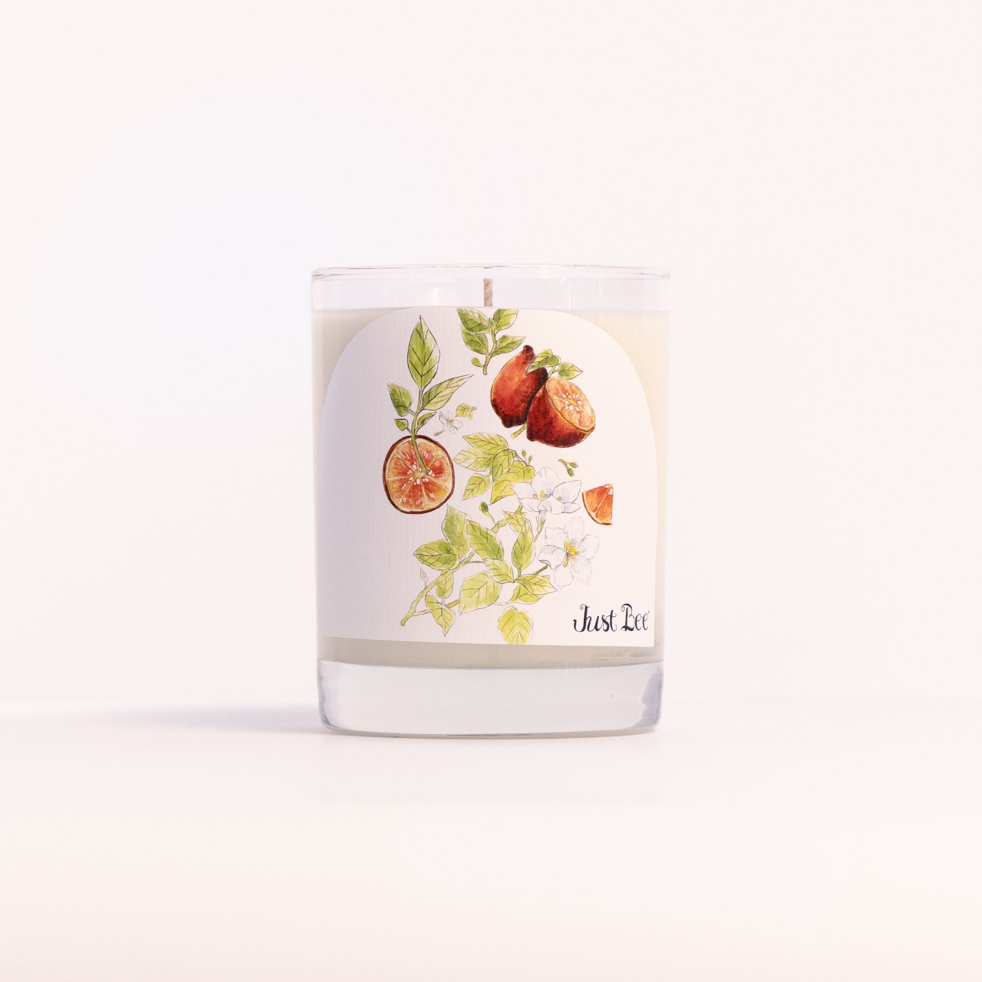 Just Bee Blood Lime & Green Tea candle in a clear glass jar illustrated with halved limes and tea leaves.