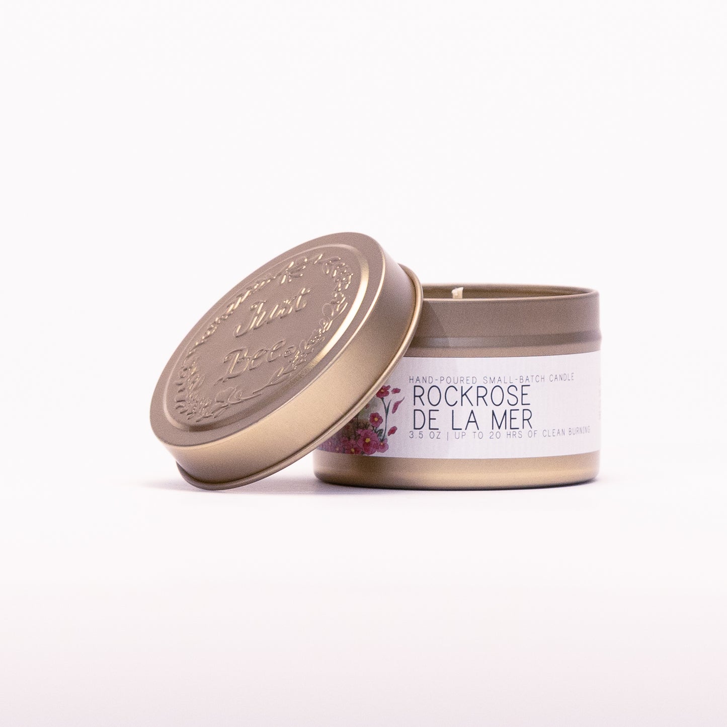 Just Bee Rockrose de la Mer travel candle in a gold tin with the embossed Just Bee lid propped against it.