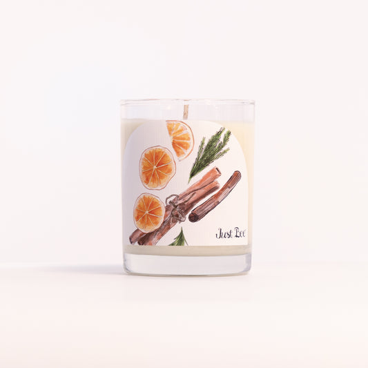 Just Bee Christmas Hearth candle in a clear glass jar illustrated with dried orange slices, cinnamon and pine.