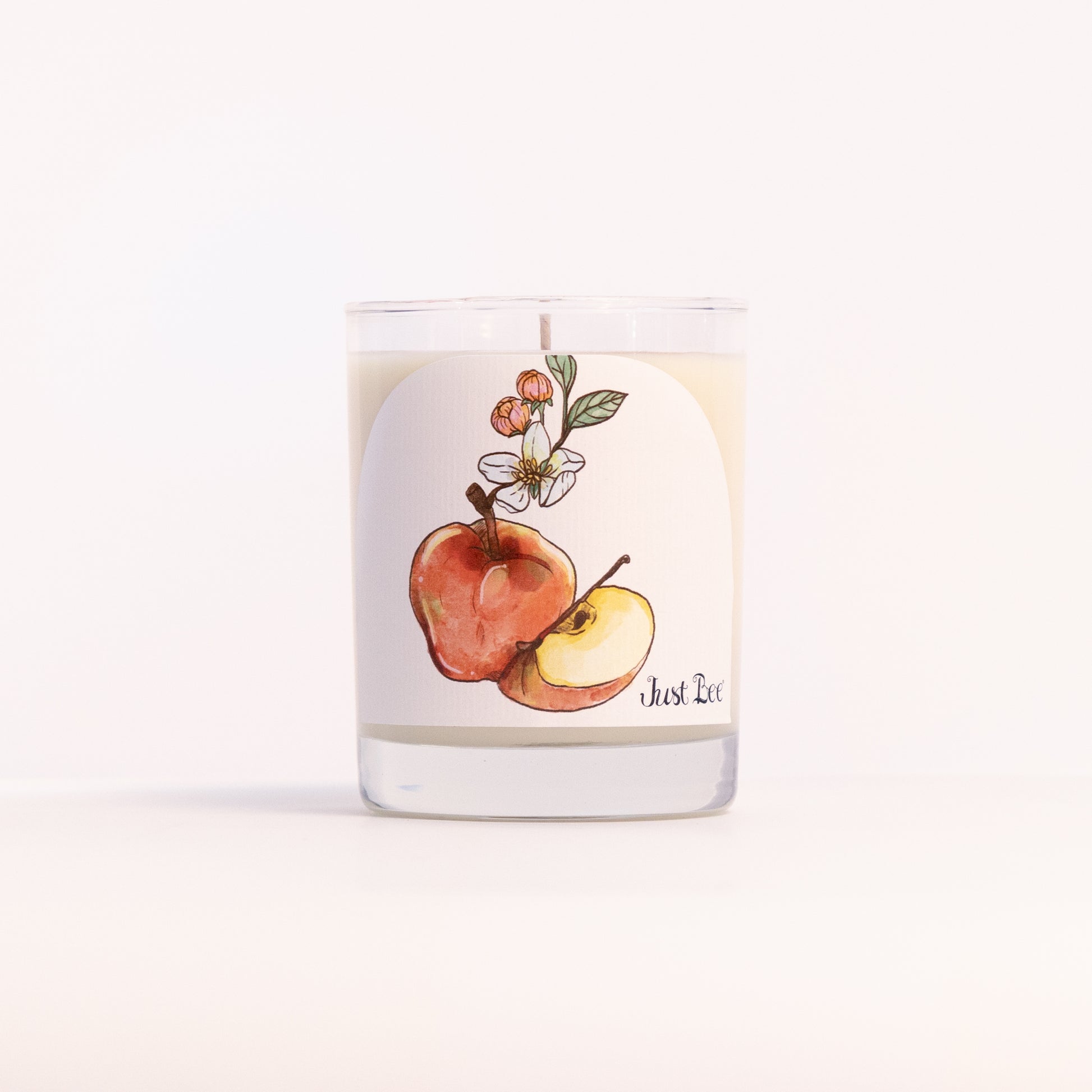 Just Bee Apple Harvest candle in a clear glass jar illustrated with red apples on a leafy branch.