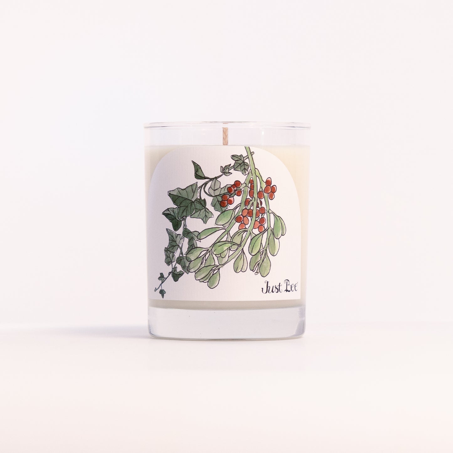 Just Bee Holly & Ivy candle in a clear glass jar illustrated with holly leaves and red berries.