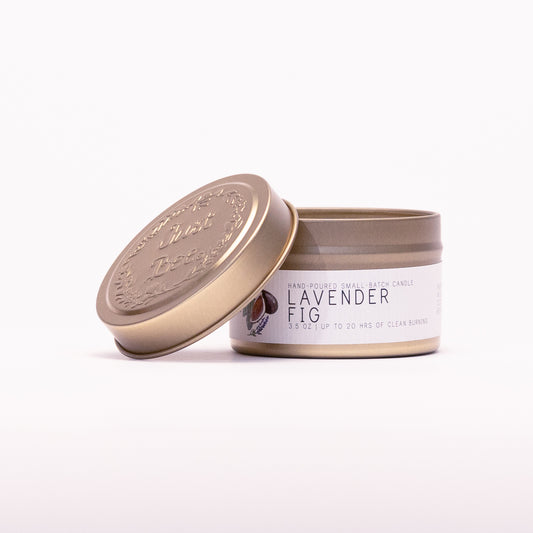 Just Bee Lavender Fig travel candle in a gold tin with the embossed Just Bee lid propped against it.