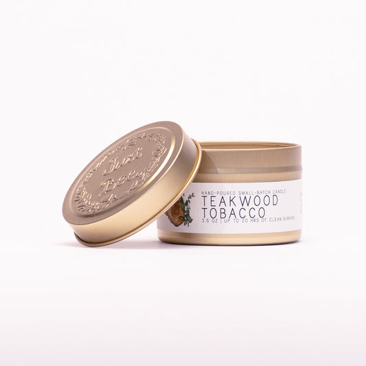 Just Bee Teakwood Tobacco travel candle in a gold tin with the embossed Just Bee lid propped against it.