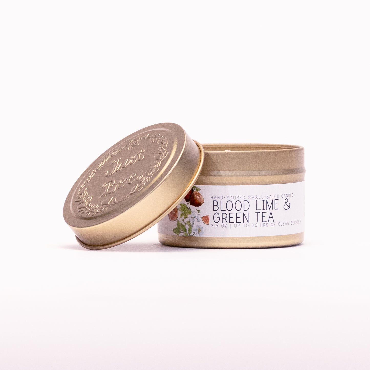 Just Bee Blood Lime & Green Tea travel candle in a gold tin with the embossed Just Bee lid propped beside it.