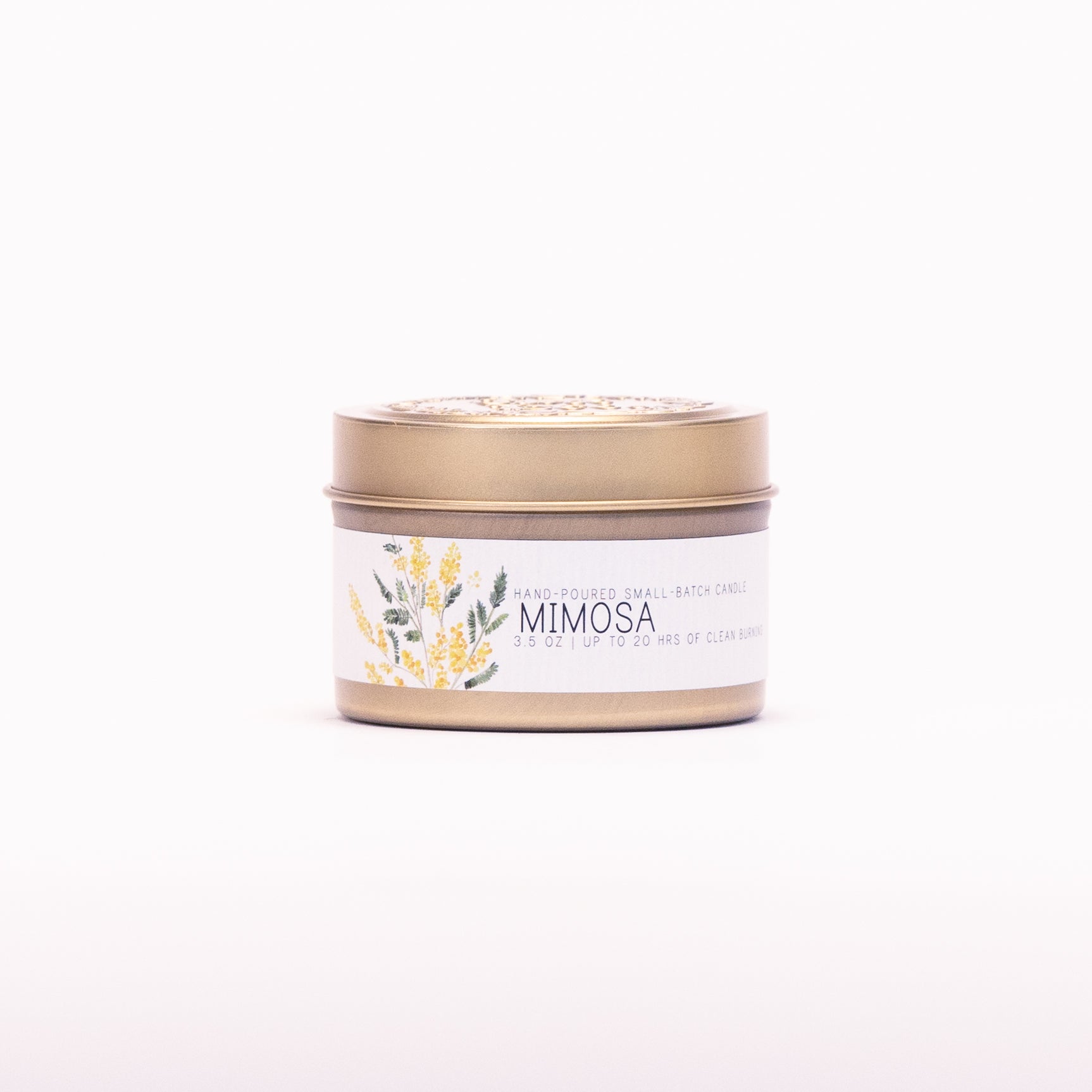 Just Bee Mimosa candle in a closed gold travel tin, yellow mimosa label facing forward.