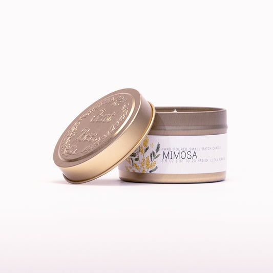 Just Bee Mimosa travel candle in a gold tin with the embossed Just Bee lid propped against it.