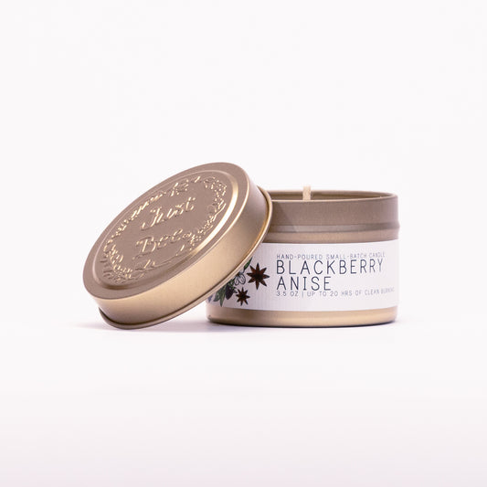 Just Bee Blackberry Anise travel candle in a gold tin with the embossed Just Bee lid propped against it.