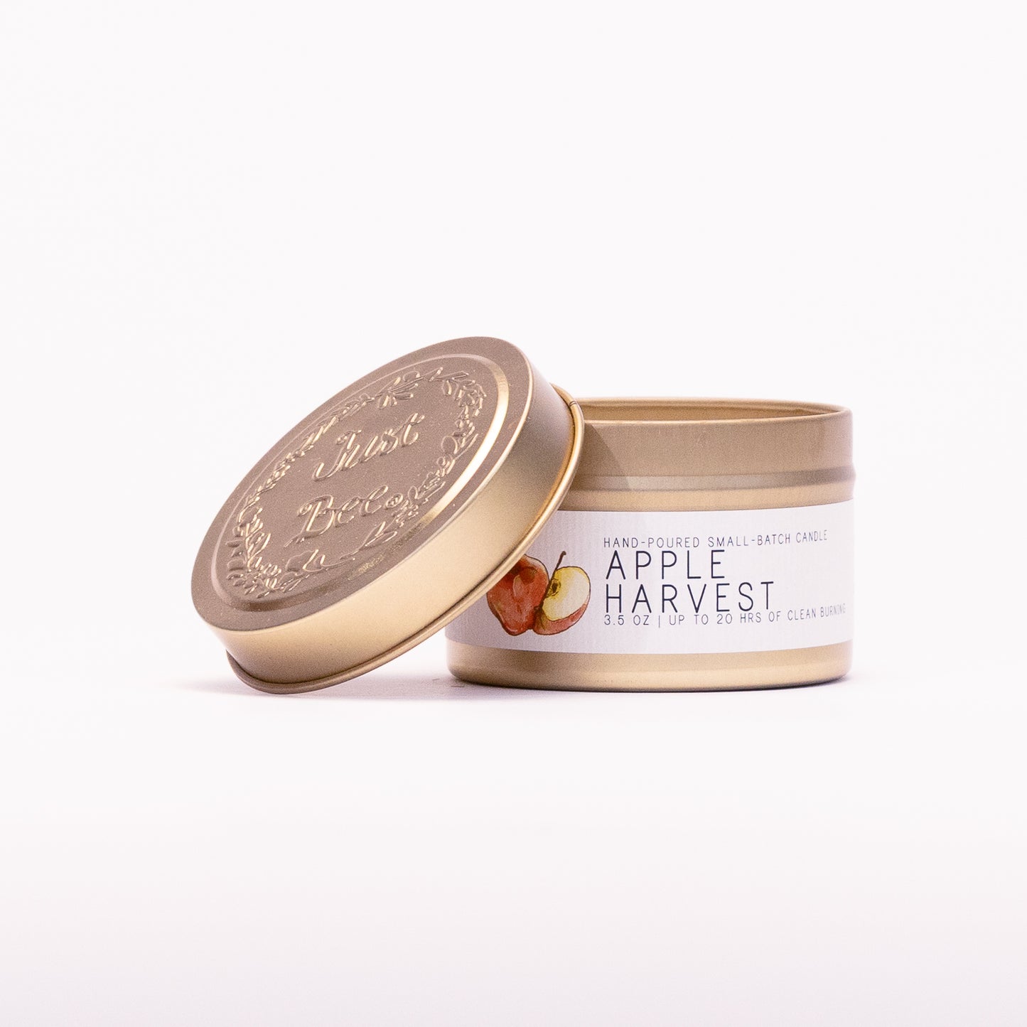 Just Bee Apple Harvest travel candle in a gold tin with the embossed Just Bee lid propped against it.