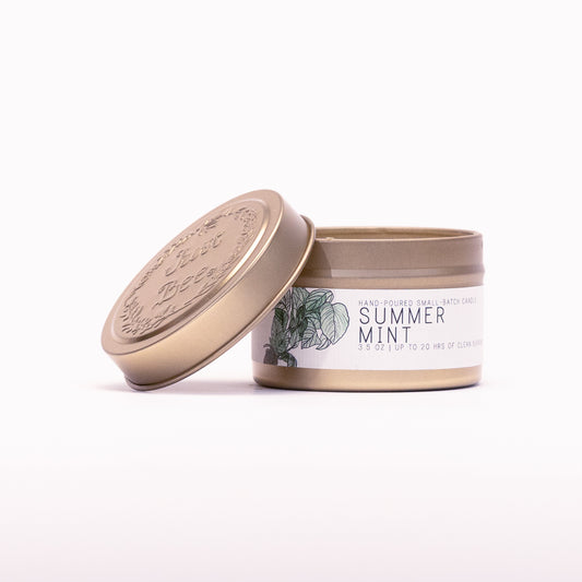Just Bee Summer Mint travel candle in a gold tin with the embossed Just Bee lid propped against it.